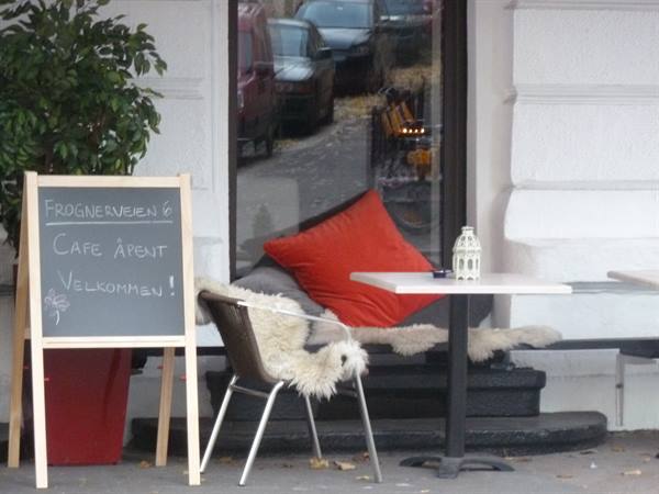 Cafe terrace with orange cushion, sheepskins and chalkboard sign at Frognerveien, Oslo