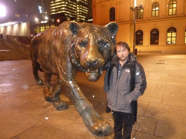 Tourist beside the bronze tiger statue outside Oslo Central Station at night