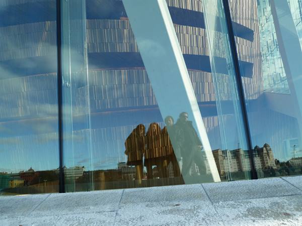 Visitors reflected on the glass facade of Oslo Opera House, city mirrored in blue