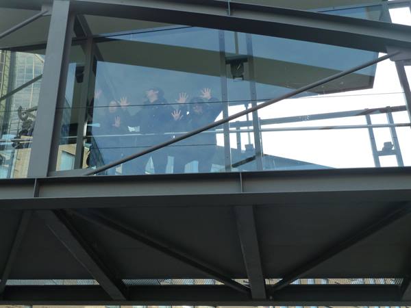 Tourists wave behind the glass walls of Oslo Opera House steel walkway