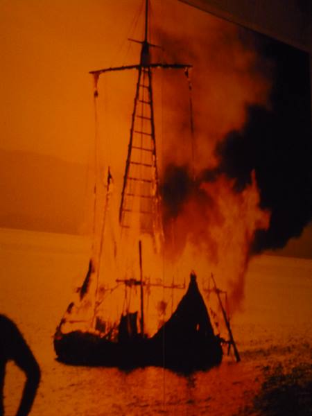 Wooden sailing ship burning on dark water, intense orange light