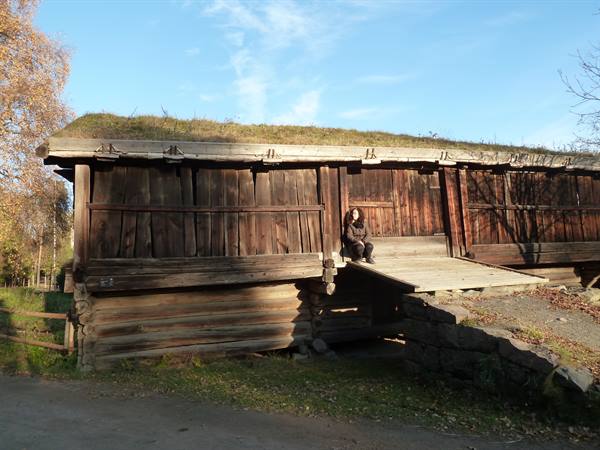 Woman sitting by an old wooden stave house with grass roof, Oslo
