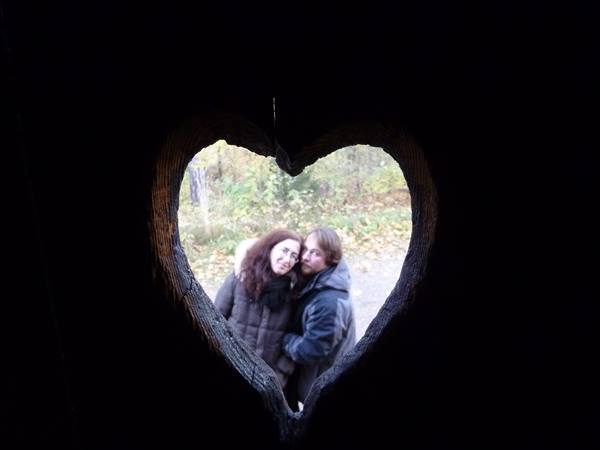 Couple framed inside a carved wooden heart, autumn forest behind them