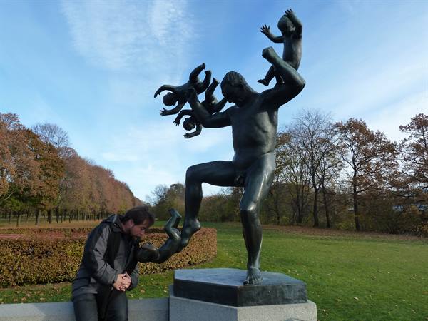 Man crouching beside Vigeland's bronze statue in Frogner Park, Oslo