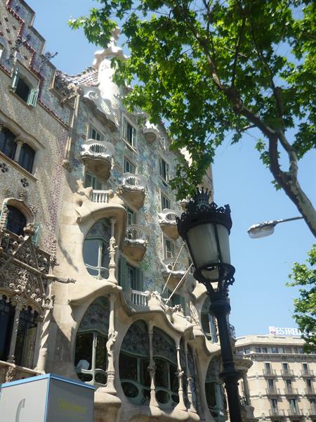 Facciata modernista di Casa Batlló tra foglie verdi e un lampione in ferro