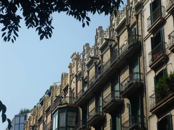 Facciata modernista con balconi in ferro battuto sotto foglie in controluce, Barcellona