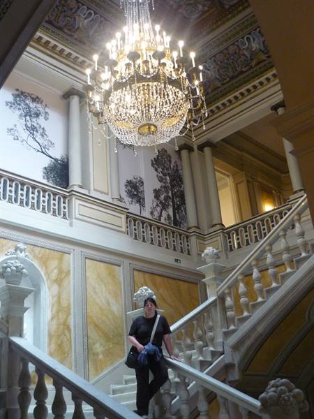 Woman on the marble staircase beneath a large crystal chandelier