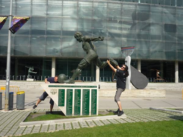 Two tourists touch the bronze footballer statue outside the stadium