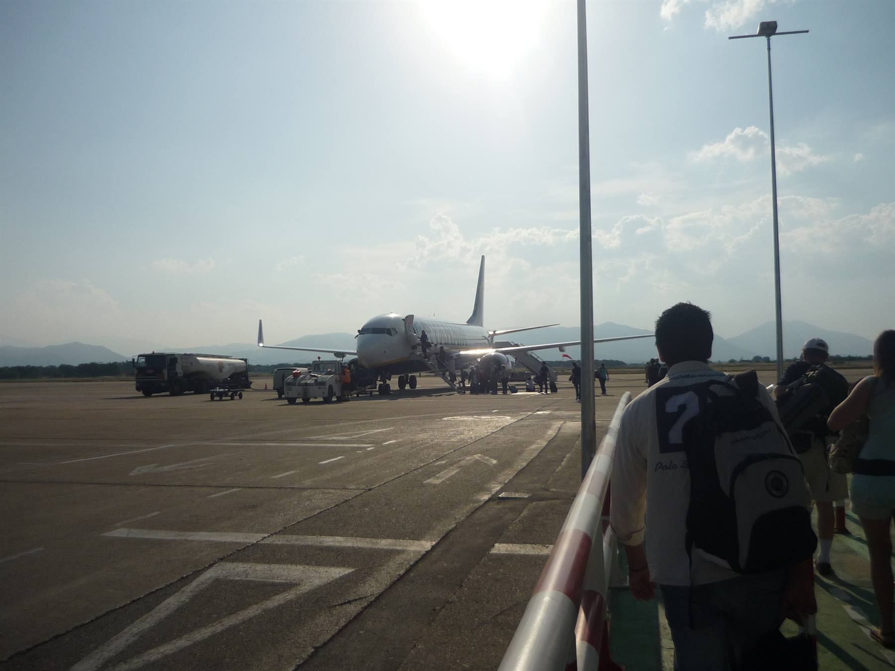 Passengers with backpack walk toward a plane on the tarmac, backlit