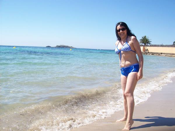 Woman in blue bikini smiles at the shoreline on a sunny beach with palm