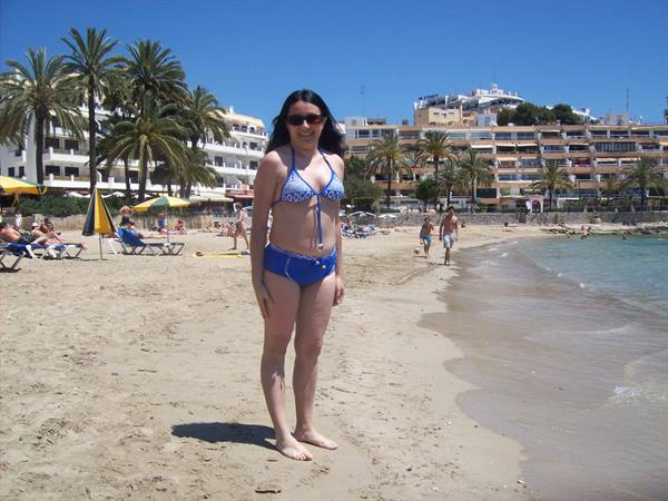 Woman in blue bikini on sandy beach, palms and hotels behind, full sun
