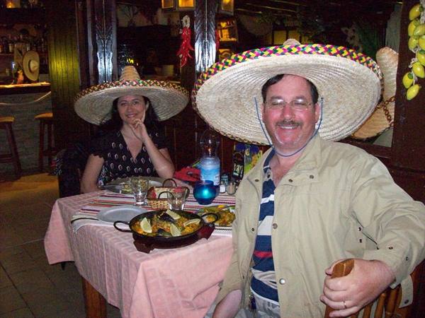 Couple wearing straw sombreros at a Mexican restaurant table with paella