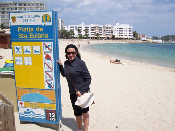 Woman next to the Platja de Sta. Eulària sign, sand and hotels behind