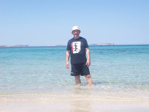 Man in hat and black T-shirt standing in clear turquoise water
