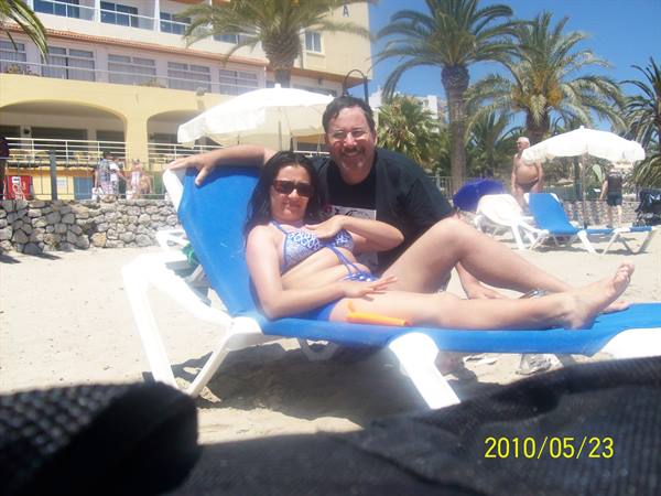 Couple in swimwear on blue sun loungers, beach with palms and hotel behind