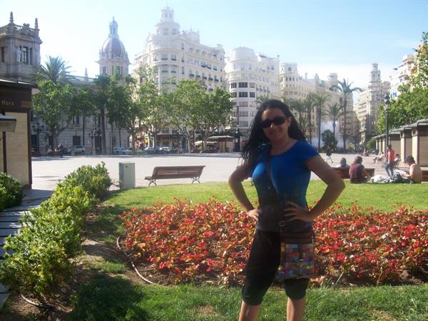 Tourist among red flowers at Valencia's Plaza del Ayuntamiento, eclectic buildings