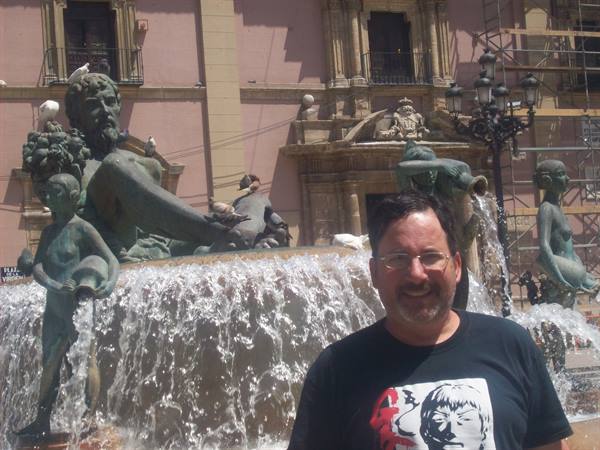 Smiling man before the bronze Turia fountain at Plaza de la Virgen, Valencia