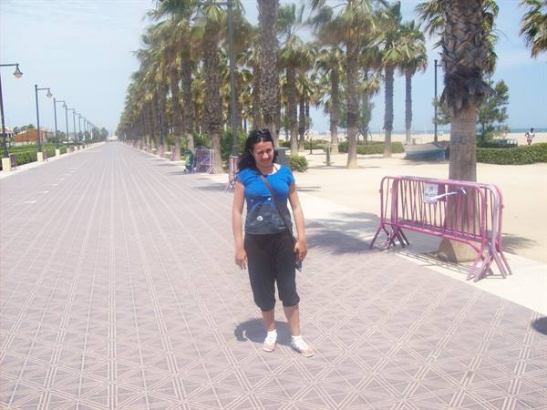 Woman in blue shirt on paved promenade lined with palm trees near the beach