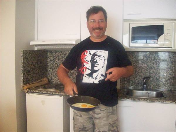Smiling man with glasses frying eggs in a small kitchen
