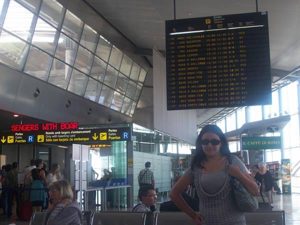 Woman in sunglasses beneath the airport departures board