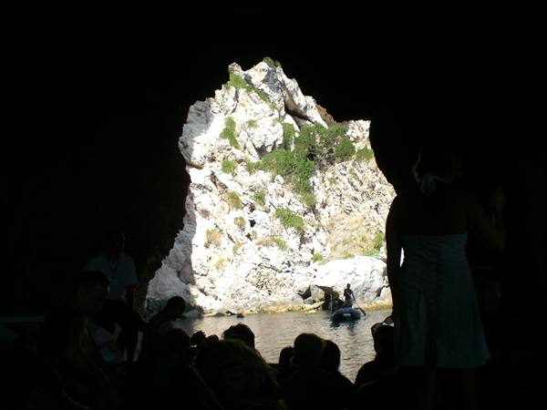 Tourists on a boat inside a dark cave, sunlit rocky entrance