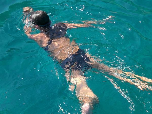 Woman wearing a mask swims in emerald sea water, sunlight sparkling on surface