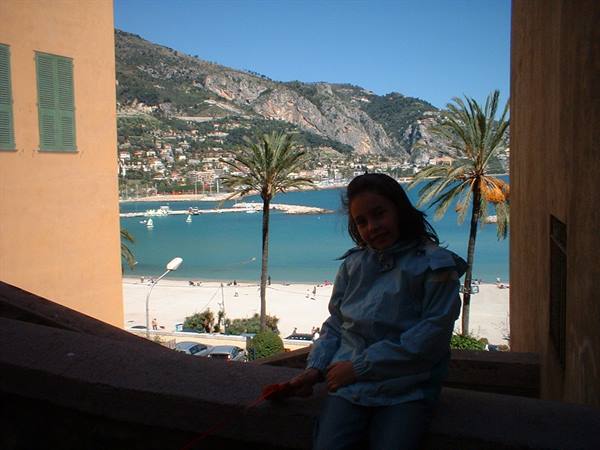 Girl sitting on stone steps, beach and palms behind in Menton