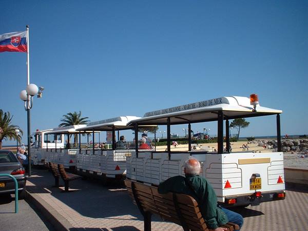 White tourist train on Le Lavandou seafront promenade, man sitting nearby
