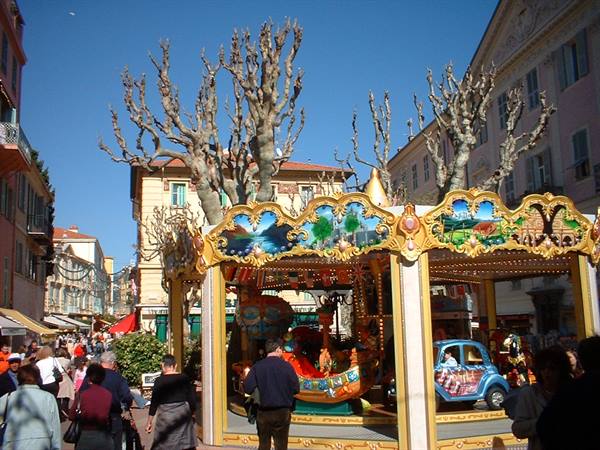 Golden carousel in a busy square with bare trees and colorful buildings