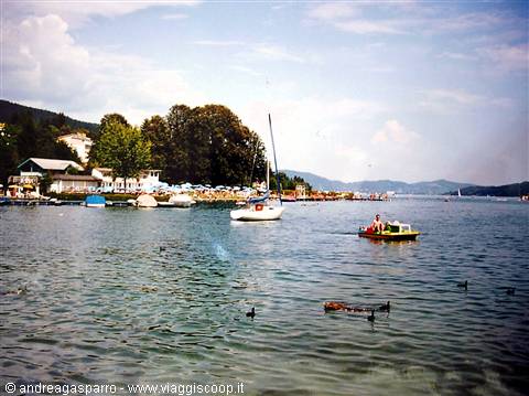 Sailboat and pedal boat on the lake, beach with umbrellas by the trees