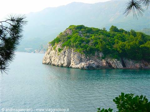 Rocky islet covered with green pines overlooks turquoise sea by misty mountains