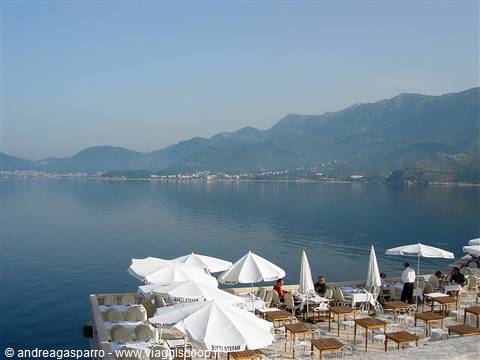 Terrace with white umbrellas and empty tables by the sea, blue mountains behind