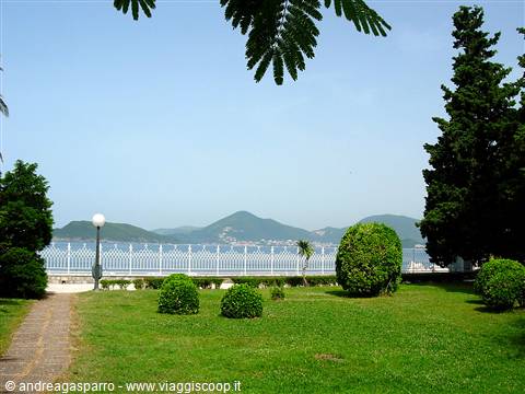 Garden with trimmed shrubs, white railing and sea behind green hills