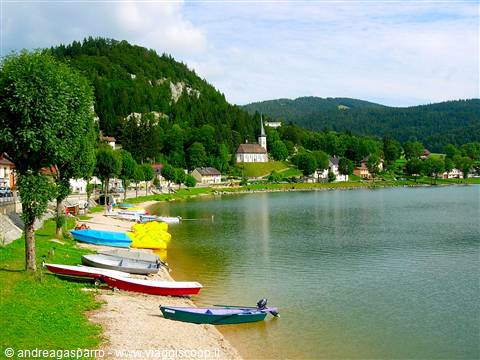 Colorful rowboats on Lake Joux shore, white church among green hills