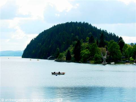 Small rowing boat on calm lake, forested hill and houses behind