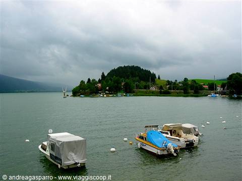Covered boats moored on the lake before a wooded hill under heavy clouds