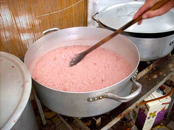 Red risotto in an aluminum pot, hand stirring with wooden spoon