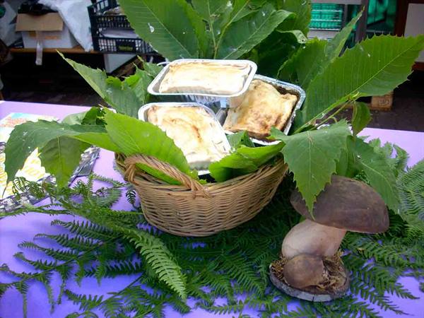 Wicker basket with savory pies in foil trays among chestnut leaves and porcini mushrooms