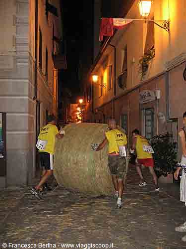Athletes push a giant hay bale through a narrow alley at night