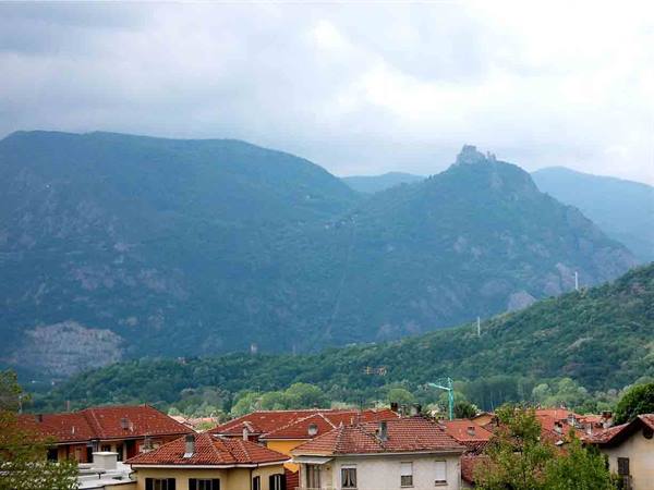 Red-tiled rooftops in front of green-blue mountains under cloudy sky