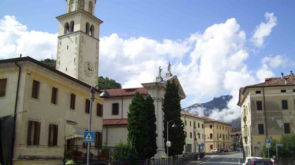 Bell tower and church among yellow houses in a square, cloudy mountains behind