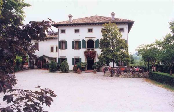 White villa with terracotta roofs, green shutters, red flowers and gravel driveway