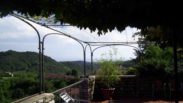 Terrace with wrought iron pergola and vines over rolling green hills, empty metal chairs
