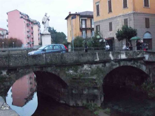 Old stone bridge with statue, cars and pedestrians under a grey sky