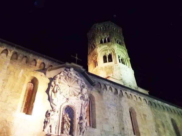 Romanesque stone church lit at night, baroque rose window and bell tower