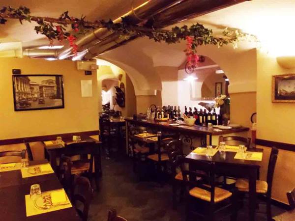 Trattoria dining room with vaulted ceilings, set tables and wine bottles at the counter