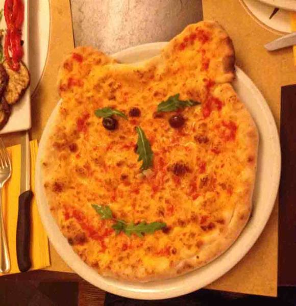 Bear-shaped pizza with arugula and olives, on a white plate in a trattoria