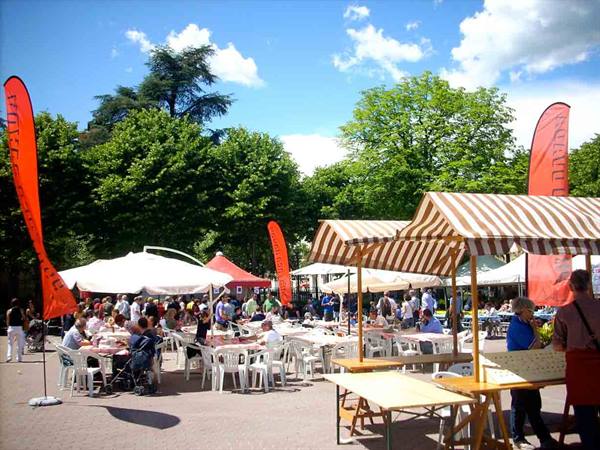 Wooden stalls and striped canopies in crowded square, people eating under umbrellas