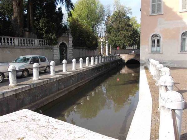 Urban canal with masonry bridge, marble bollards and parked cars