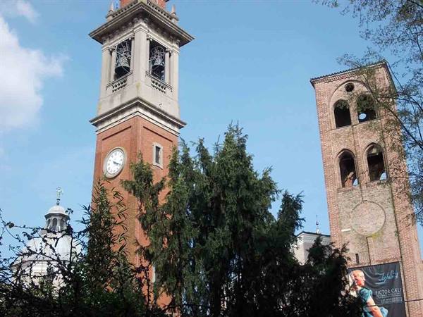Brick bell tower with clock beside ancient medieval tower, green trees, blue sky